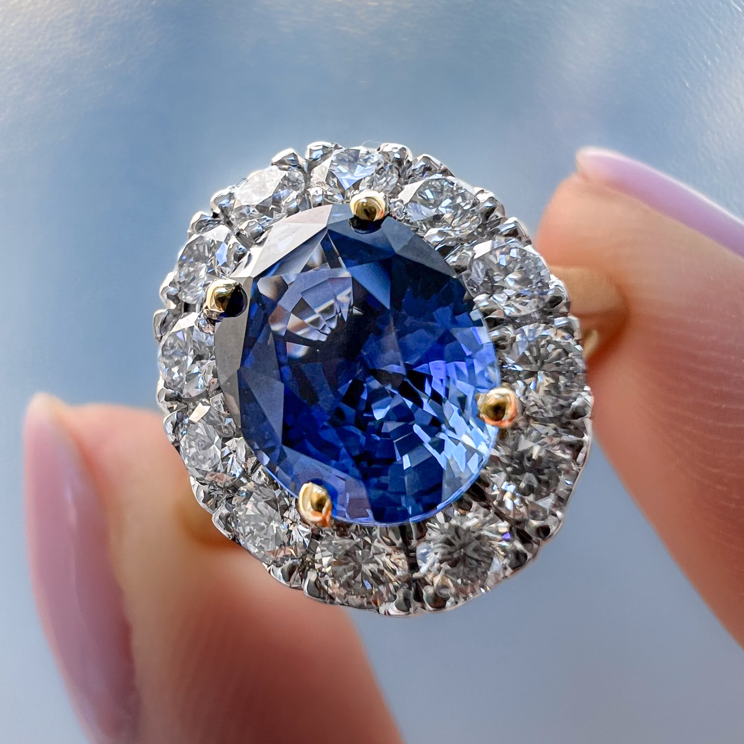 Sapphire and diamond bespoke cluster engagement ring held between finger and thumb